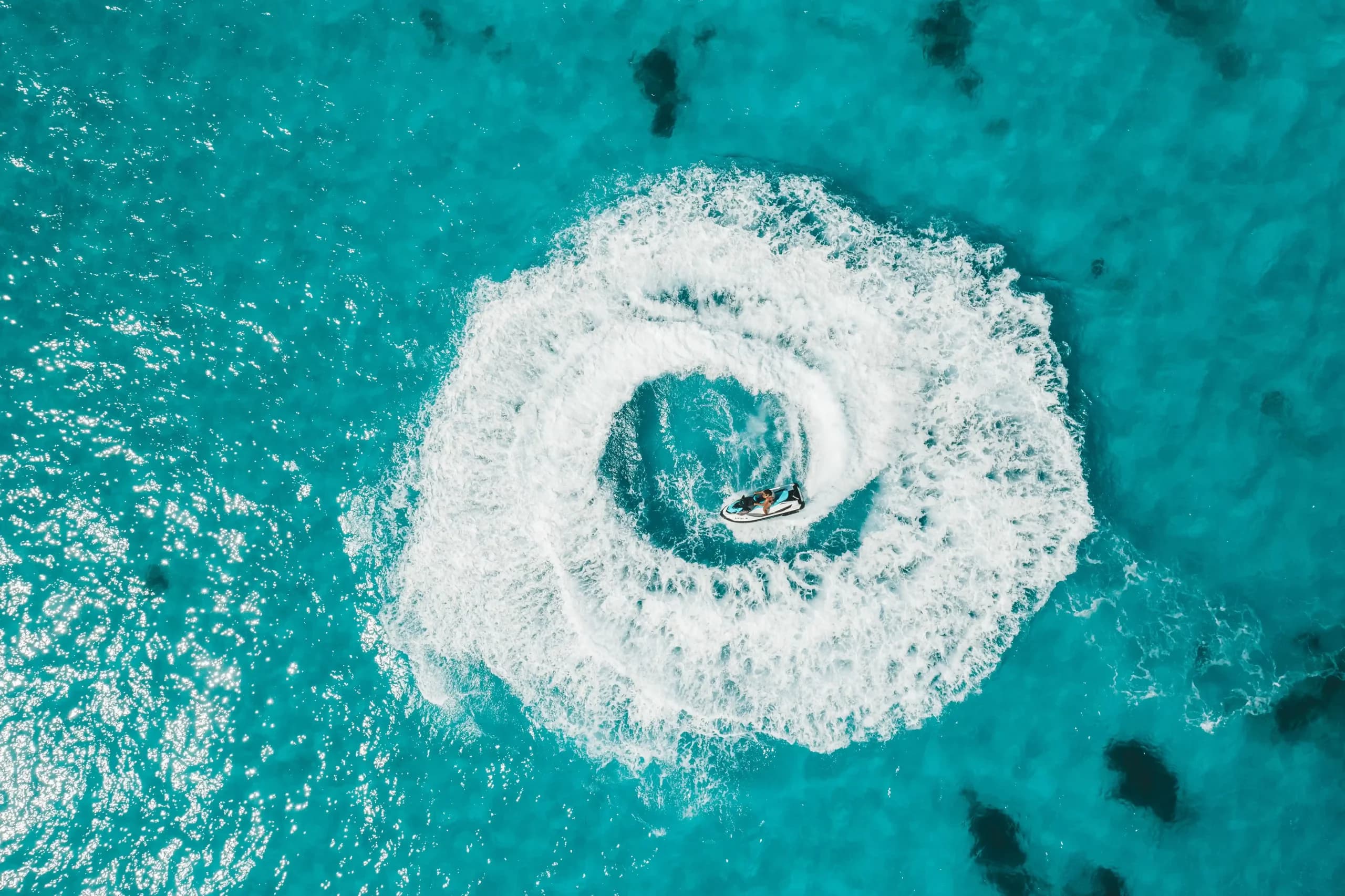 Vista aérea de una moto de agua dibujando una estela circular sobre agua mediterránea profunda